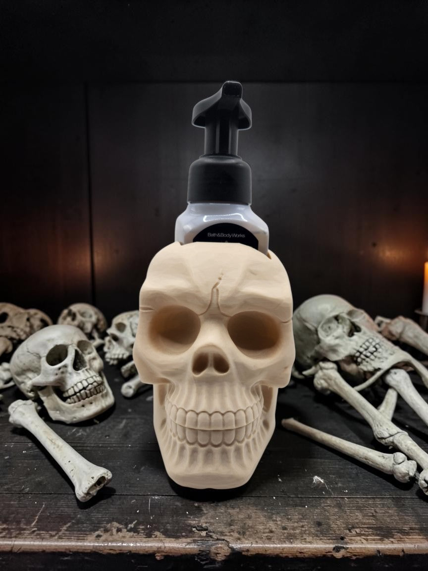 Absolute Prints bone-colored skull-shaped soap dispenser holder for foaming hand soap on a dark gothic background